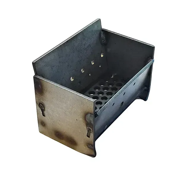 Small metal charcoal grill with perforated base and side handles on a white background