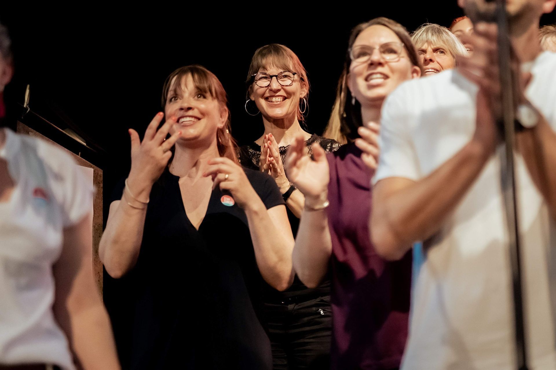 Eine Gruppe von weiblich gelesenen Personen singen und klatschen  zusammen auf einer Bühne.