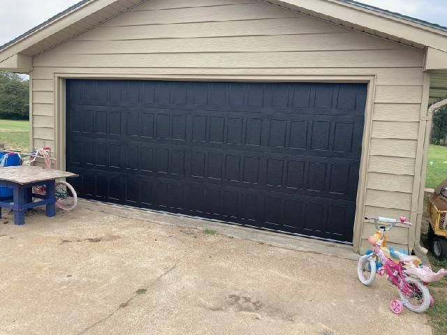Single-car garage with a black door, beige siding, and children’s toys on the driveway