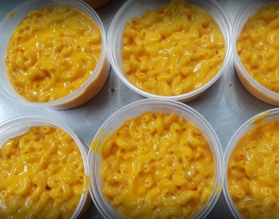 Macaroni and cheese in clear, round plastic containers. Yellow pasta, creamy sauce.