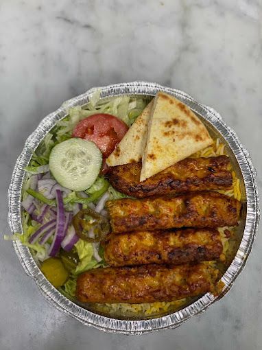 Grilled kebab dish with rice, salad, pita bread, and vegetables in a foil container.