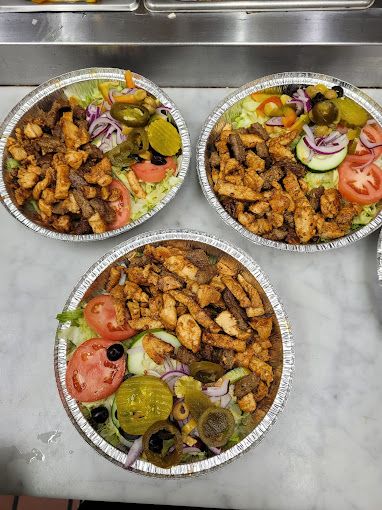 Three aluminum plates of food: chicken and beef with salad and toppings.