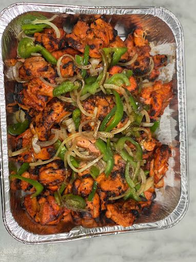 Tray of vibrant orange-red chicken pieces with green peppers and onions.