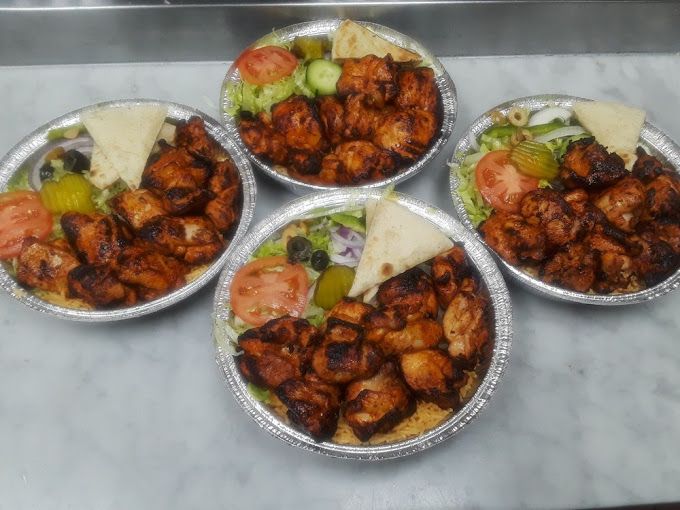 Four plates of grilled chicken with salad and pita bread, in a restaurant setting.