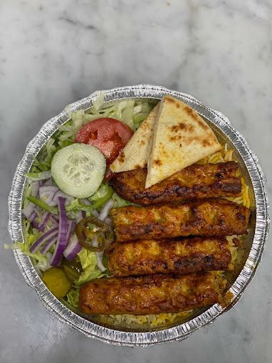 Kabob dish with grilled meat, pita bread, salad, and rice in a foil container.