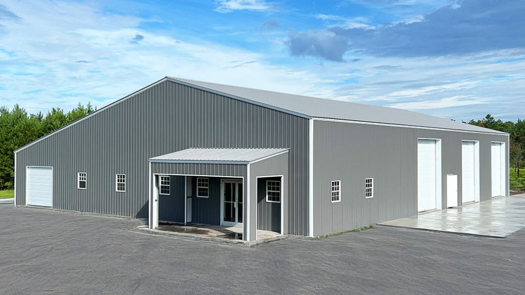 A large, modern metal building with garage doors, lit from within, dusk setting.