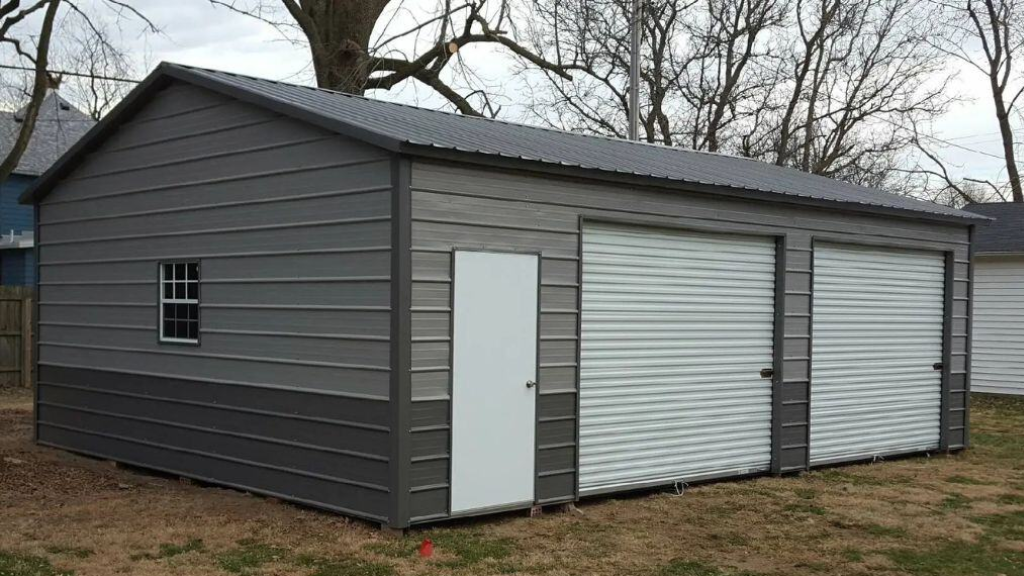 Gray metal garage with two garage doors, a window, and a side door on a concrete pad.
