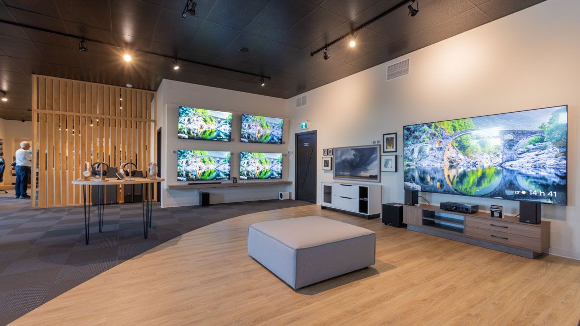 Une salle d'exposition présentant de grands téléviseurs sur les murs et les tables, avec un mobilier et un éclairage