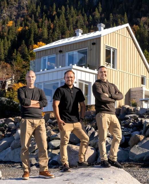 Trois hommes debout devant une maison moderne ; des montagnes en arrière-plan.