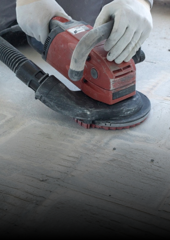 Gloved hands using a red orbital sander on a concrete surface