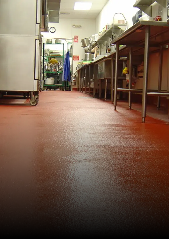 Narrow commercial kitchen with stainless steel counters and a red floor, viewed from a low angle