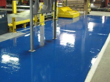 Blue epoxy factory floor with yellow safety barriers and industrial equipment