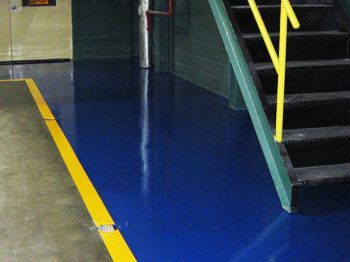 Blue floor with a yellow safety line beside a stairway and railing indoors