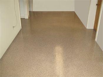 Empty hallway with beige speckled floor and white walls, viewed toward a closed doorway.