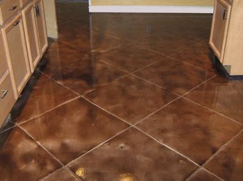 Brown tiled kitchen floor with diagonal grout lines between light wood cabinets