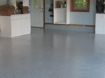Empty garage with gray floor, white cabinets, and a door opening to the outside.