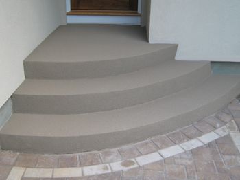 Curved concrete steps leading to a doorway beside a tiled walkway