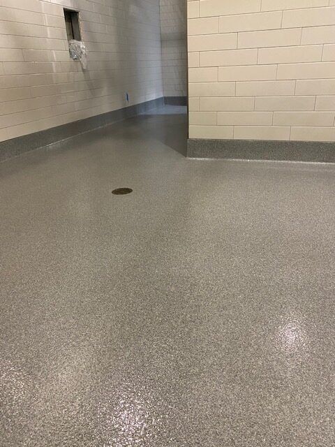 Empty indoor hallway with beige brick walls and a gray speckled floor