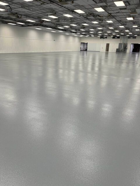 Empty indoor warehouse with a polished gray floor and rows of ceiling lights