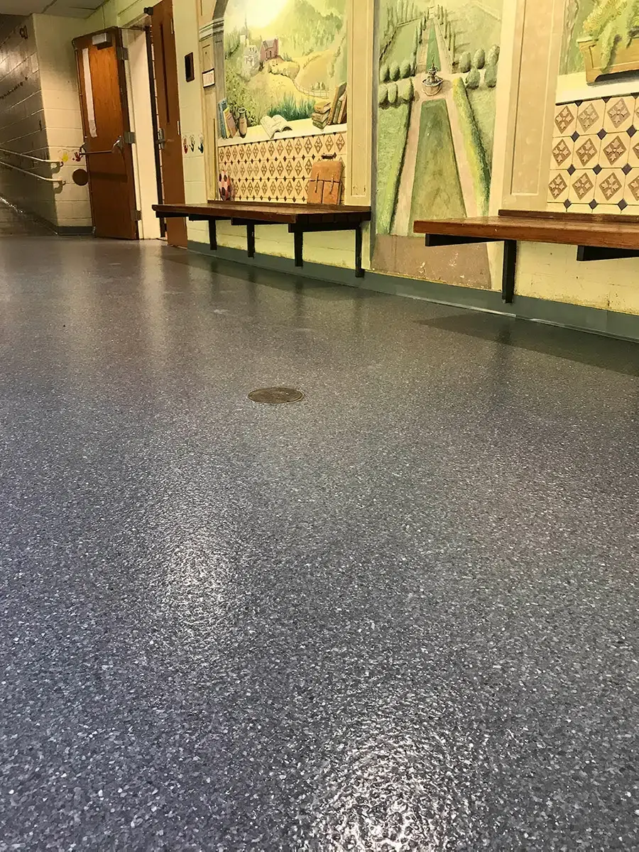 Empty indoor hallway with blue speckled floor, wall murals, and benches along the side