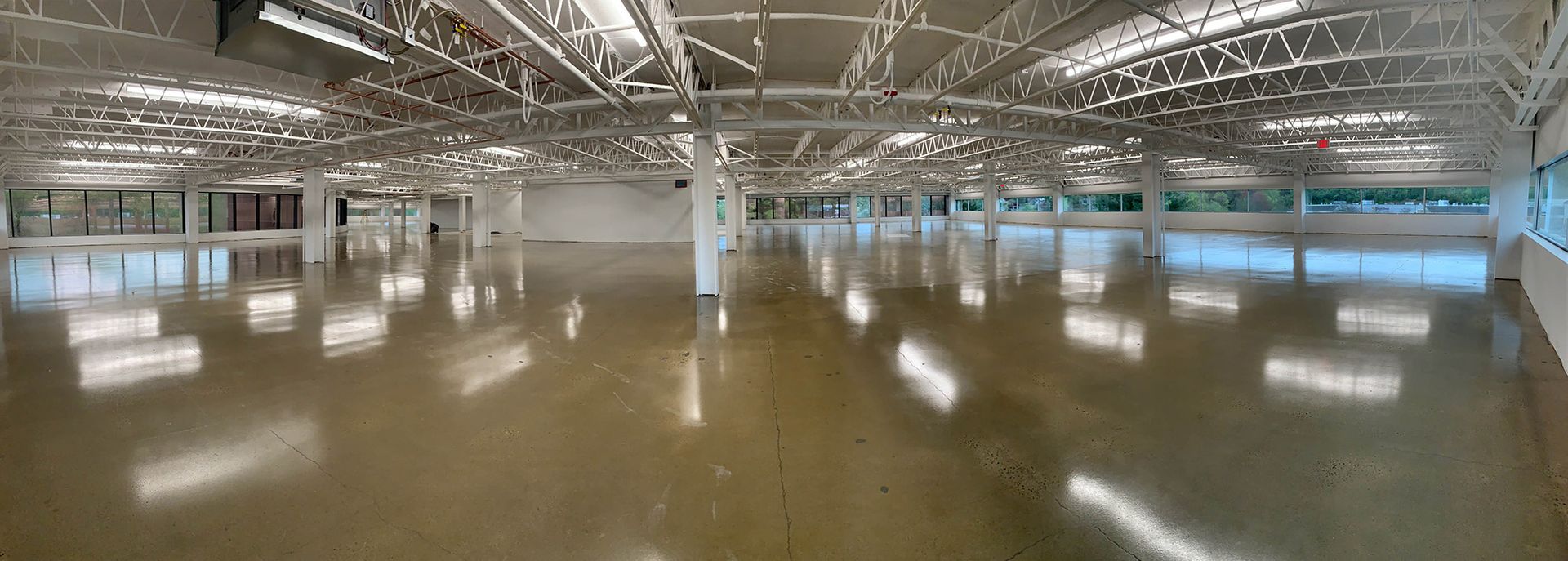 Empty indoor gymnasium with polished floor, white columns, and high metal ceiling