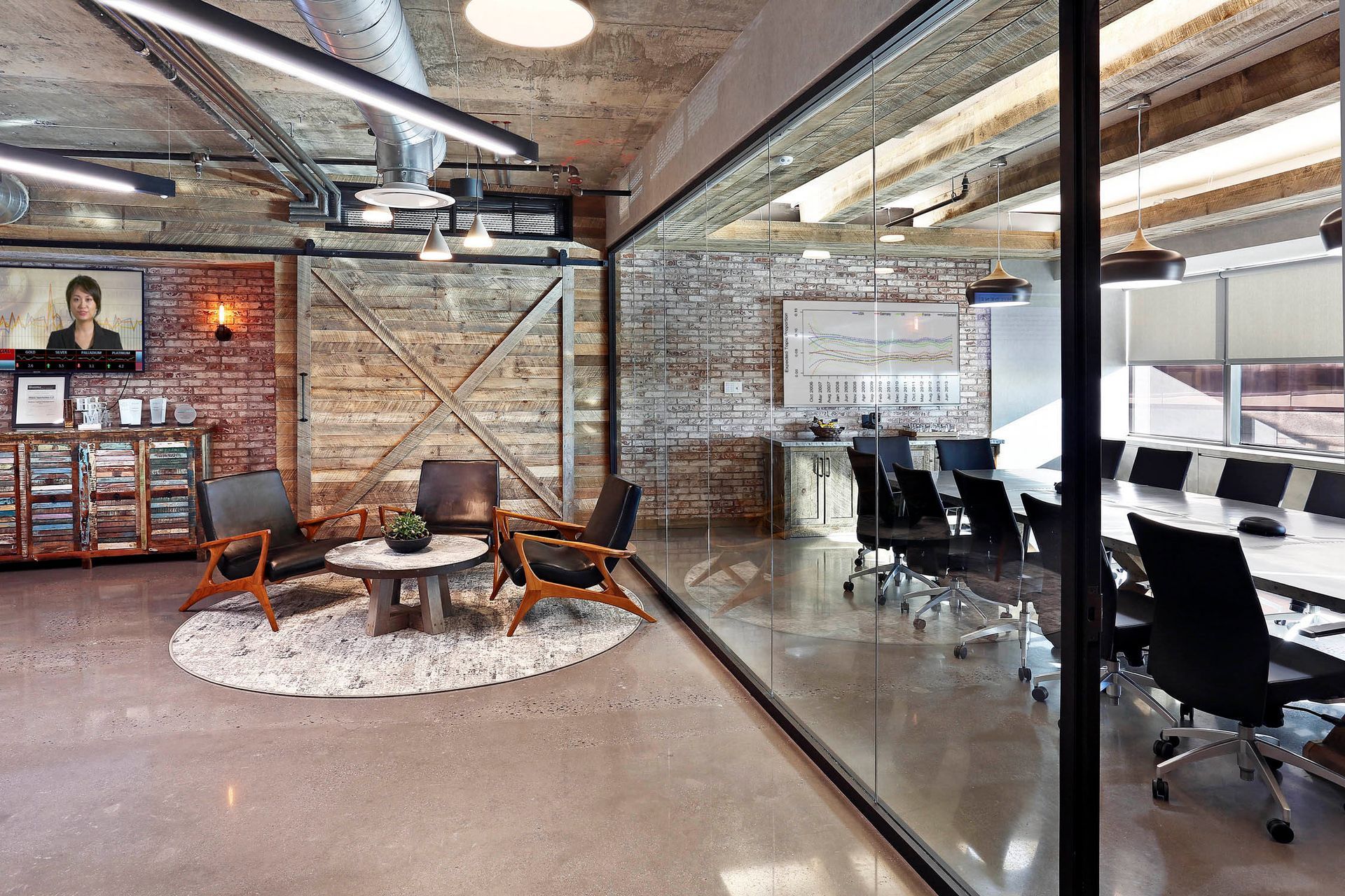 Modern industrial office lounge with seating area, glass-walled conference room, and exposed brick decor.