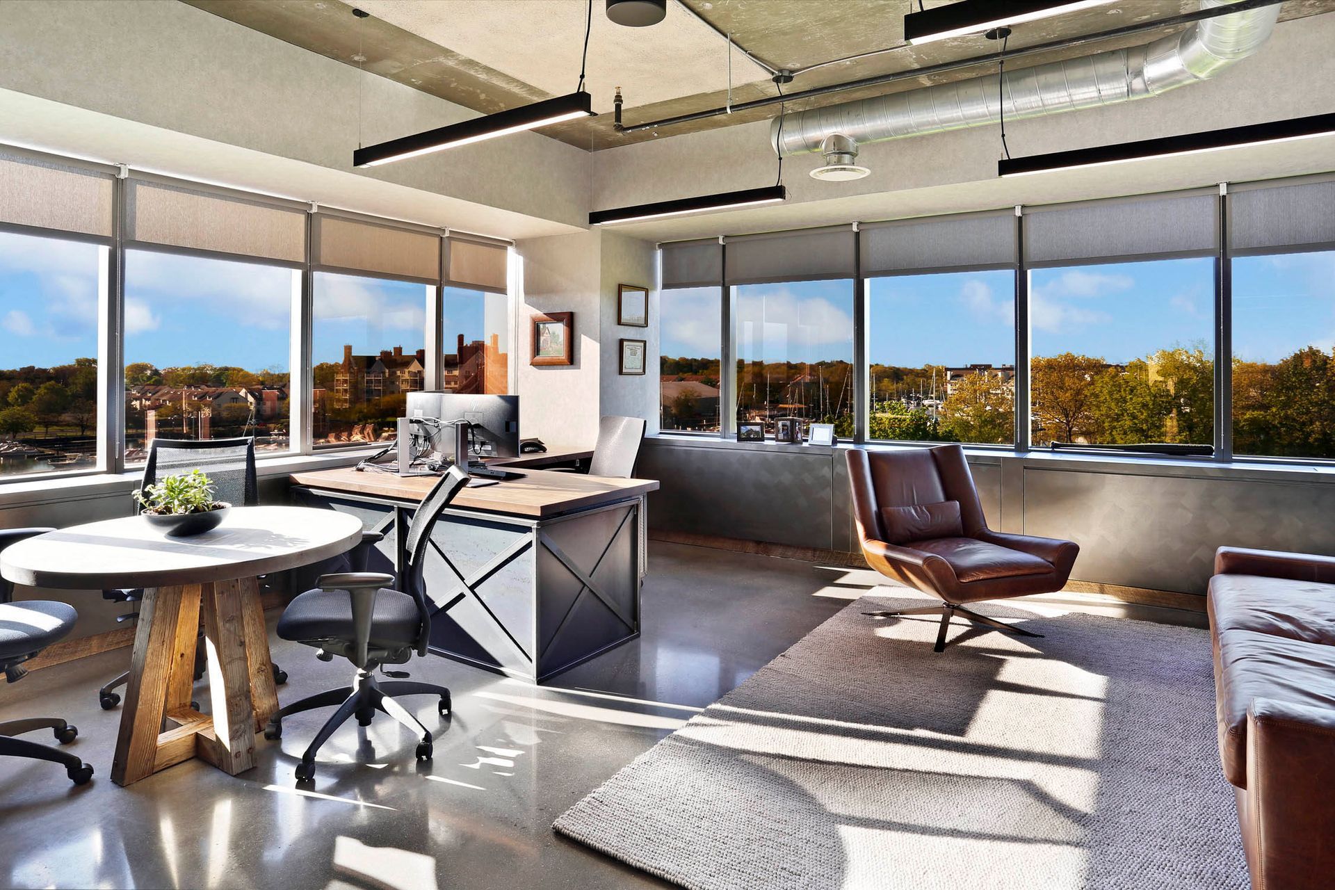 Modern loft office with large windows, desk chairs, and sunlight on a gray carpet