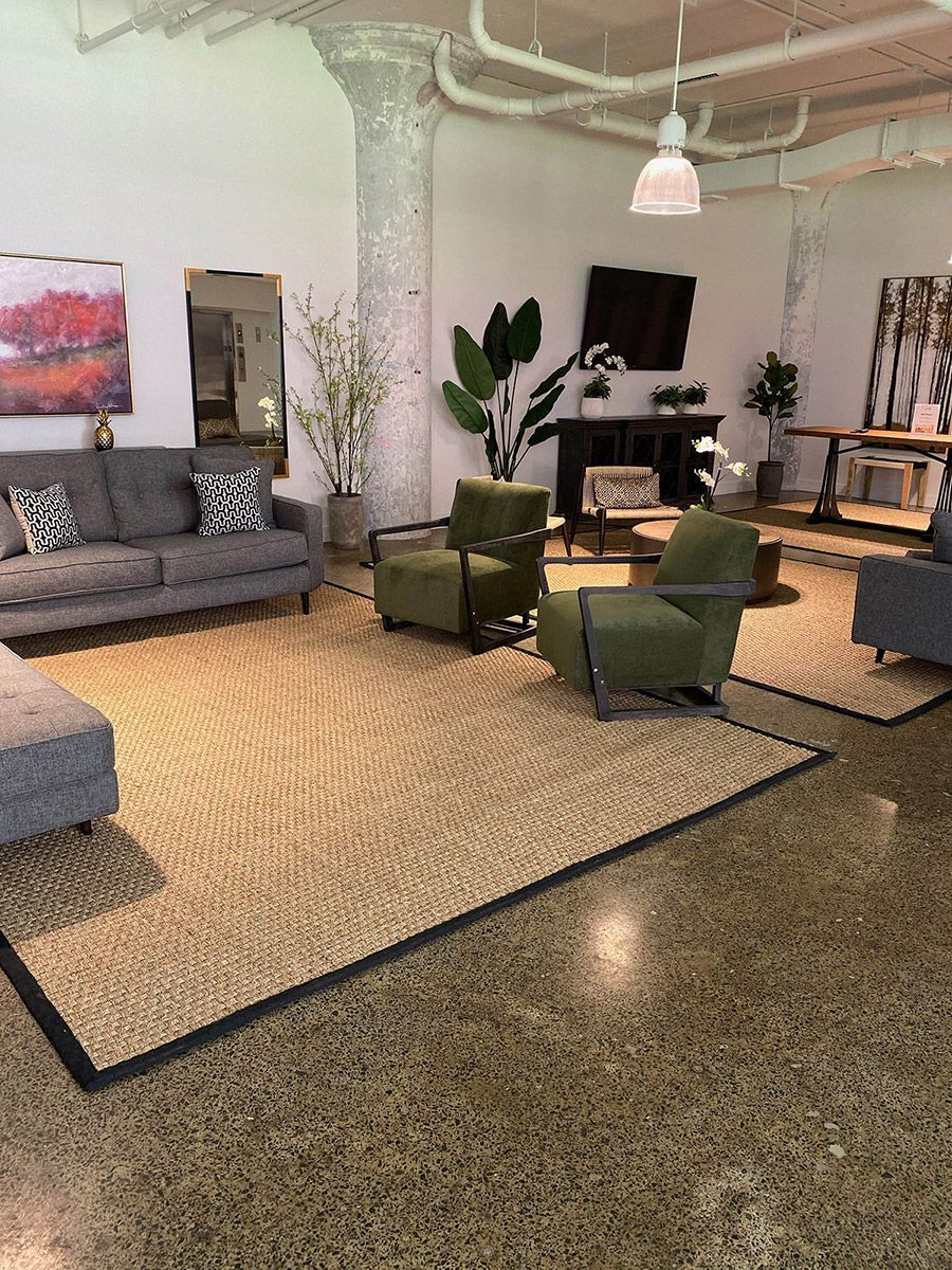Modern lounge with gray sofa, green chairs, rug, desk, and polished floor under white columns