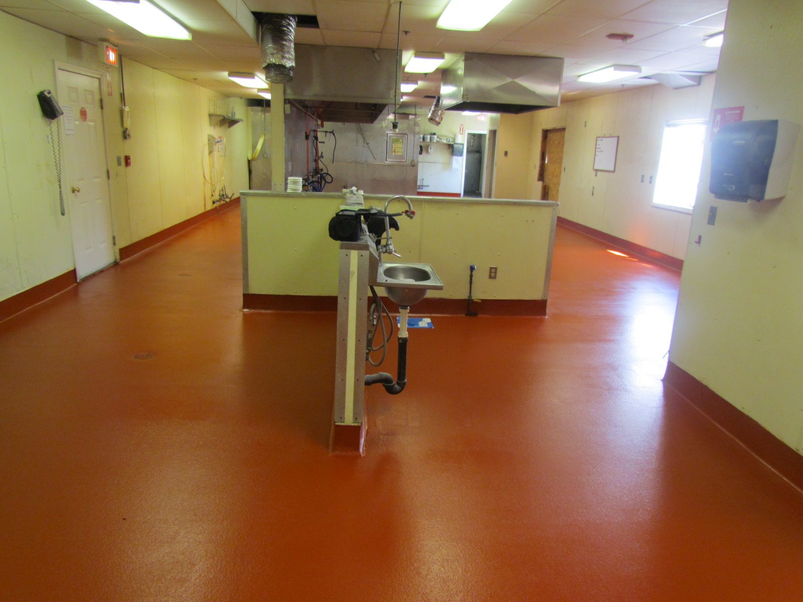 Bright indoor corridor with orange floor, cream walls, and a central turnstile or barrier gate