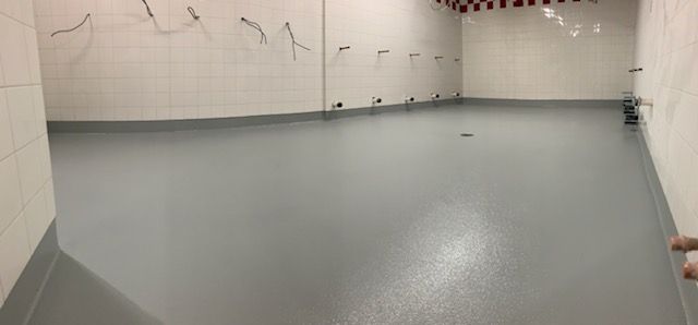 Empty tiled shower room with gray floor, white walls, and wall-mounted shower heads