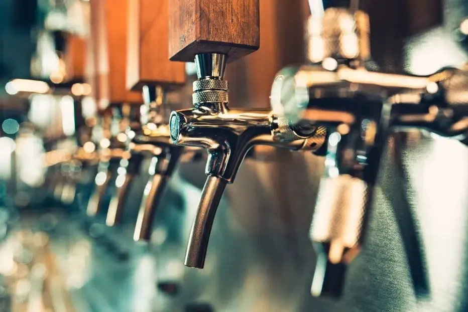 Row of beer taps on a bar counter, with a warm, blurred background