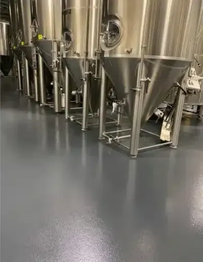 Stainless steel industrial tanks with conical bottoms in a clean factory room with gray flooring