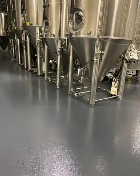 Stainless steel brewing tanks on a smooth gray factory floor.