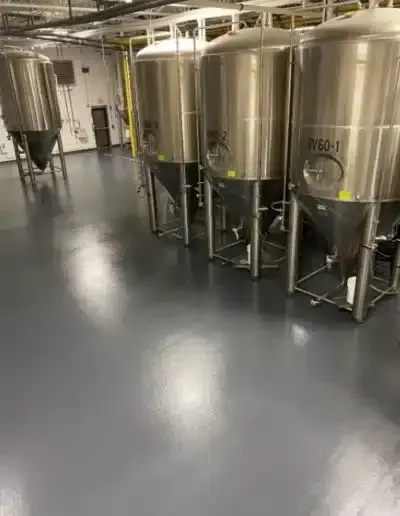 Stainless steel industrial tanks lined up in a clean facility with a gray floor and white ceiling pipes