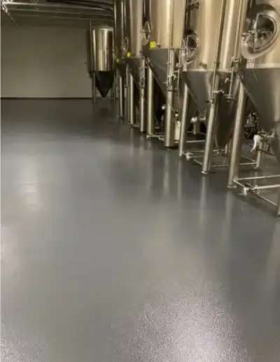 Row of stainless steel brewing tanks in an industrial facility with a polished concrete floor