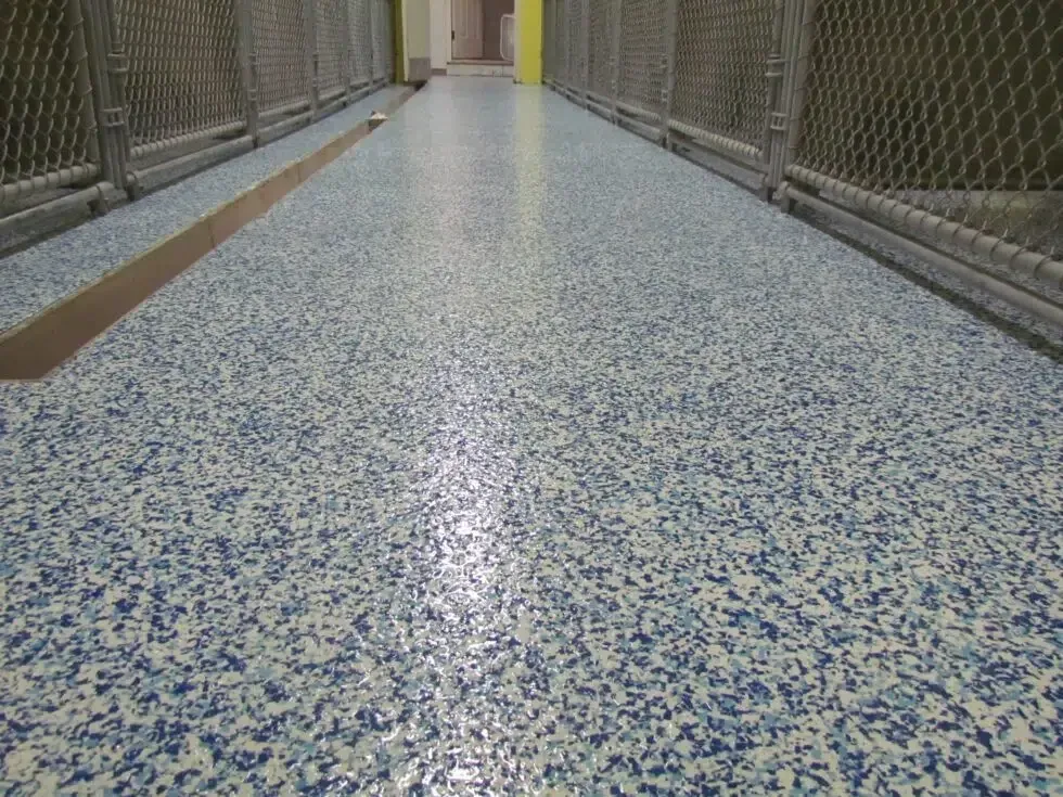 Narrow hallway with blue-speckled terrazzo floor and chain-link fencing on both sides