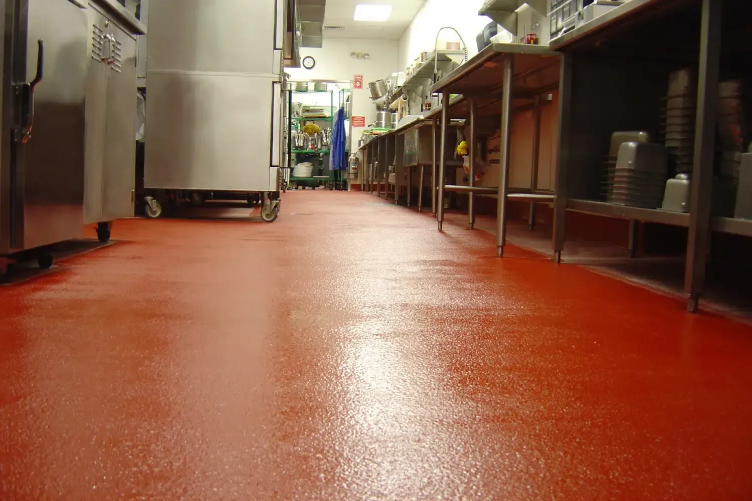 Commercial kitchen with a red floor, stainless steel counters, and shelves lining a narrow aisle