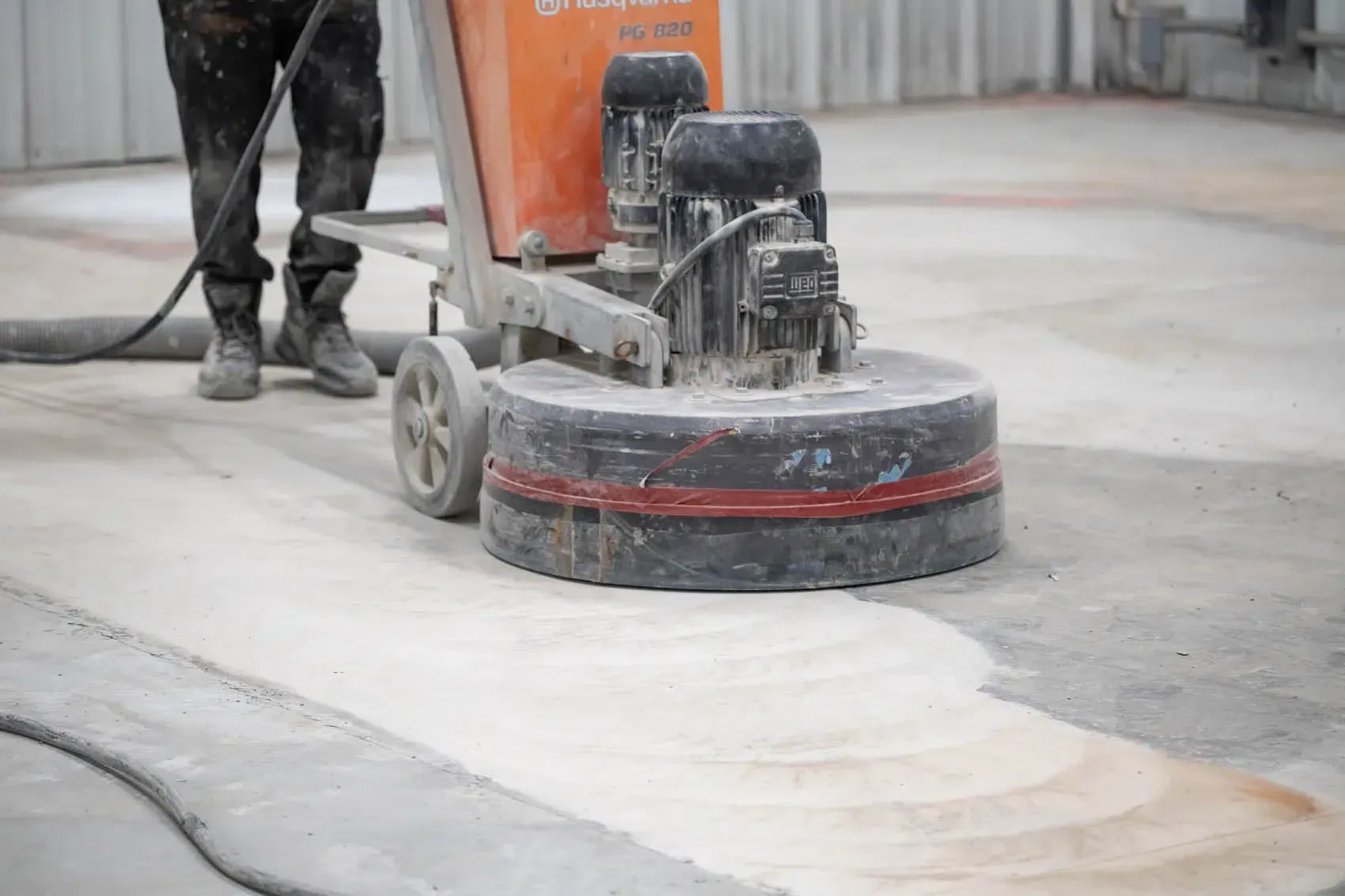 Worker using a floor grinder to smooth a dusty concrete surface in a construction area
