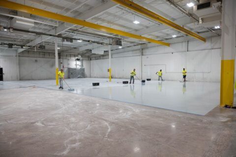 Workers installing a large white floor in an empty industrial warehouse