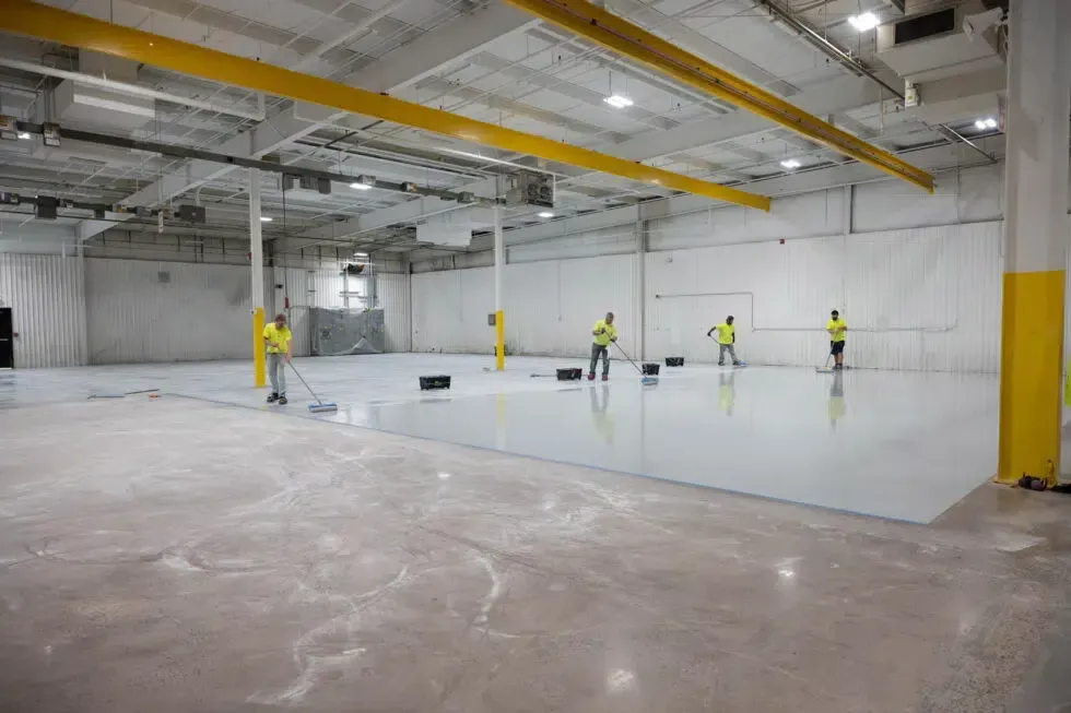 Workers in yellow vests installing a large indoor floor in a warehouse-like space