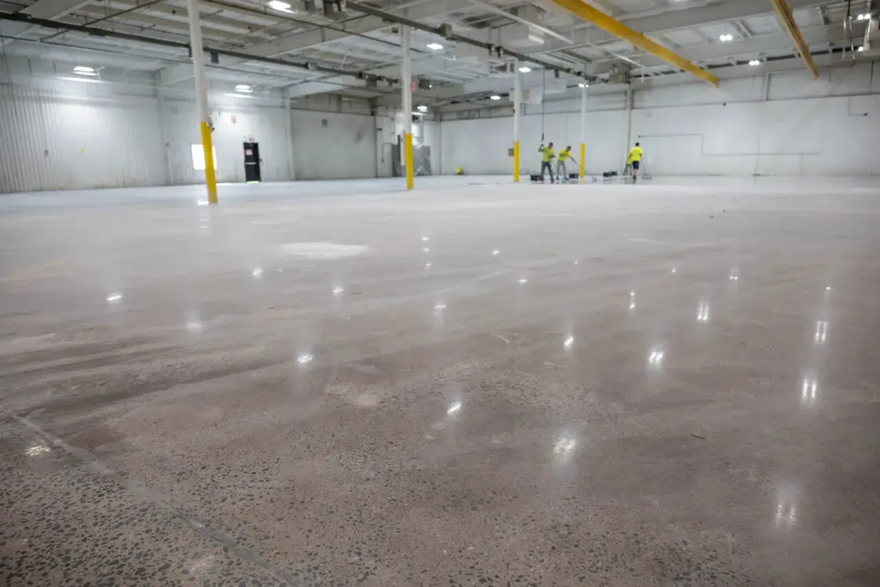 Large empty warehouse with a polished concrete floor and workers in yellow safety gear in the distance