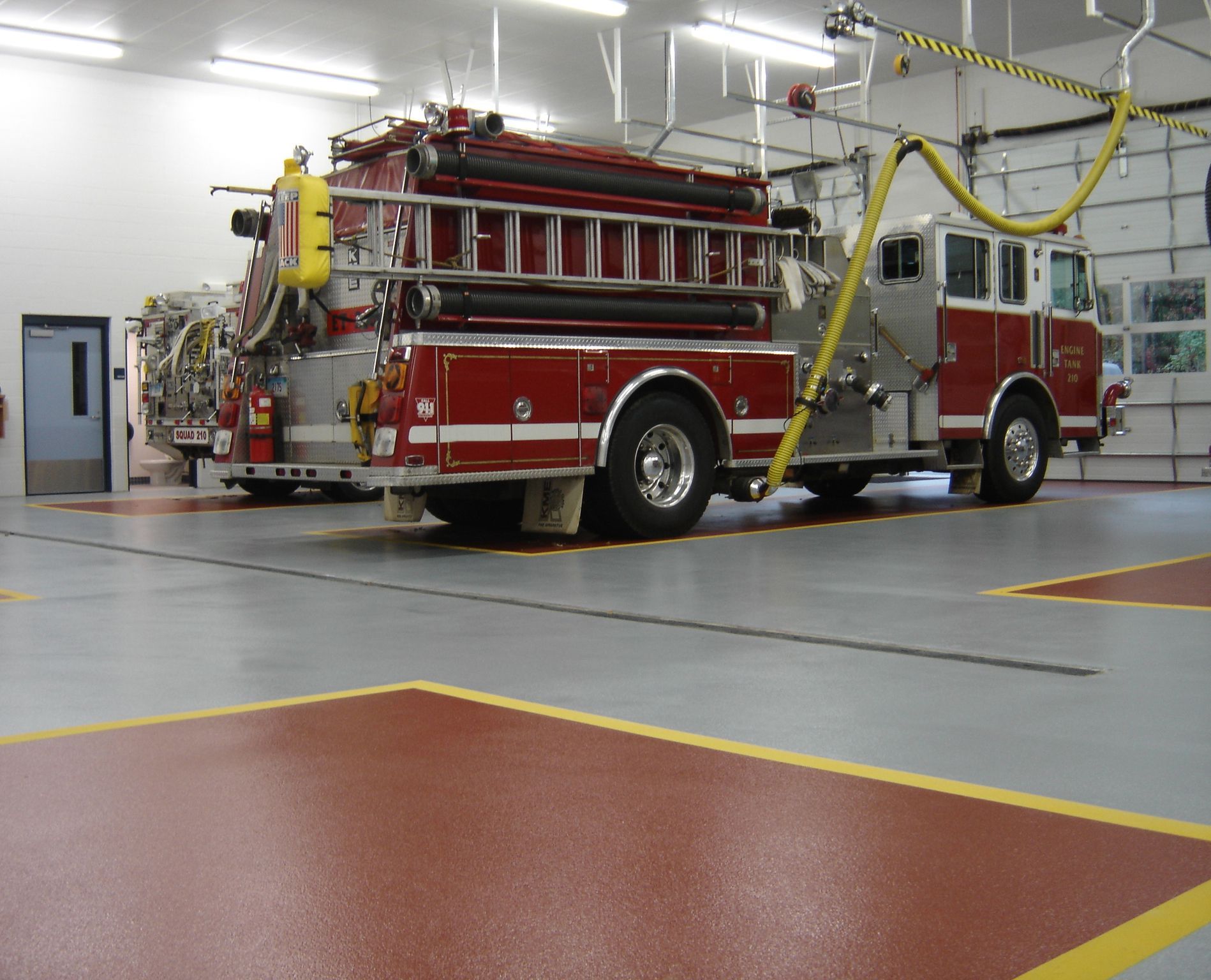 Red fire truck parked inside a fire station garage under bright lights.