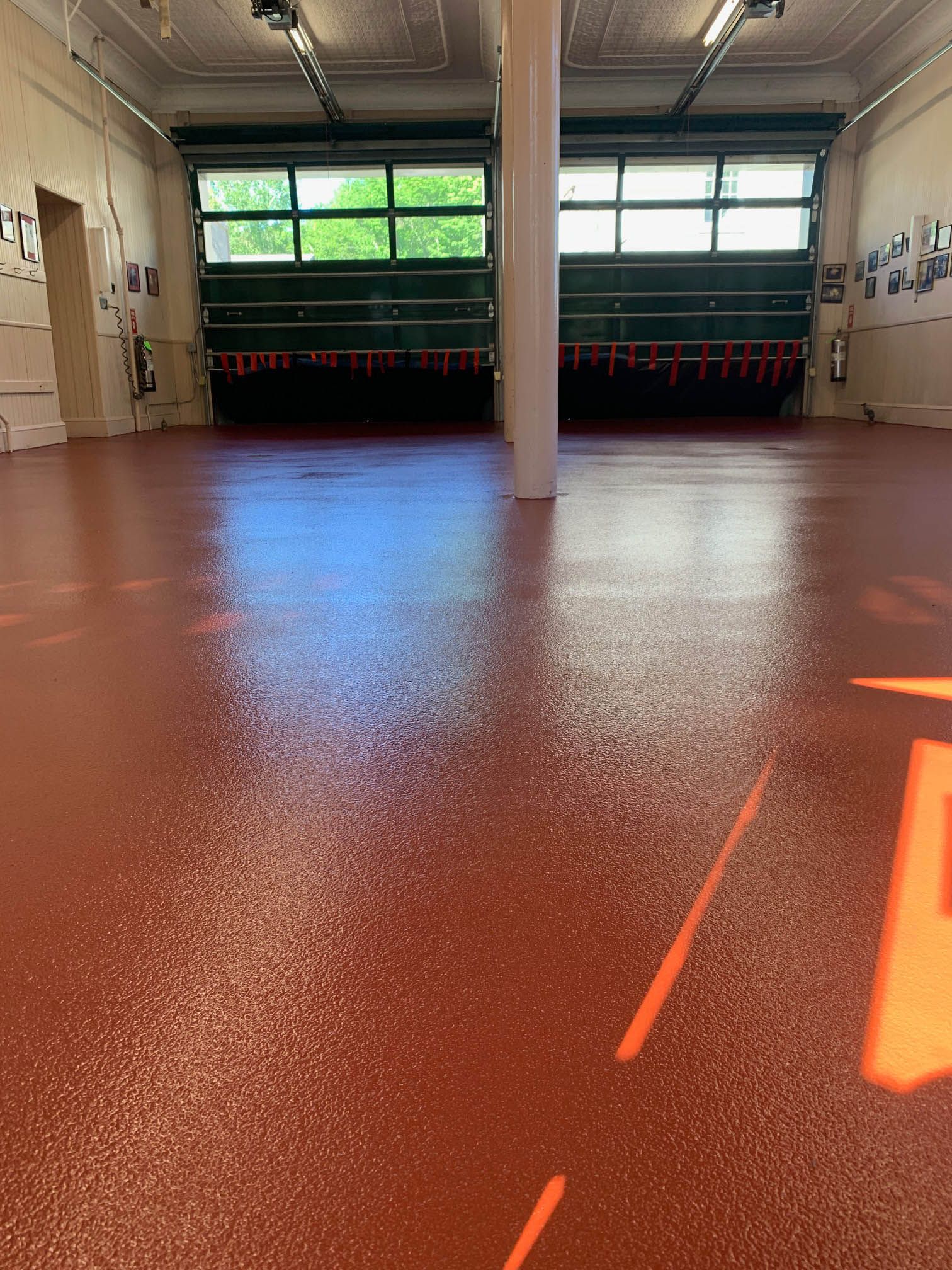 Empty indoor gym with a shiny red floor, windows at the back, and a central support pillar