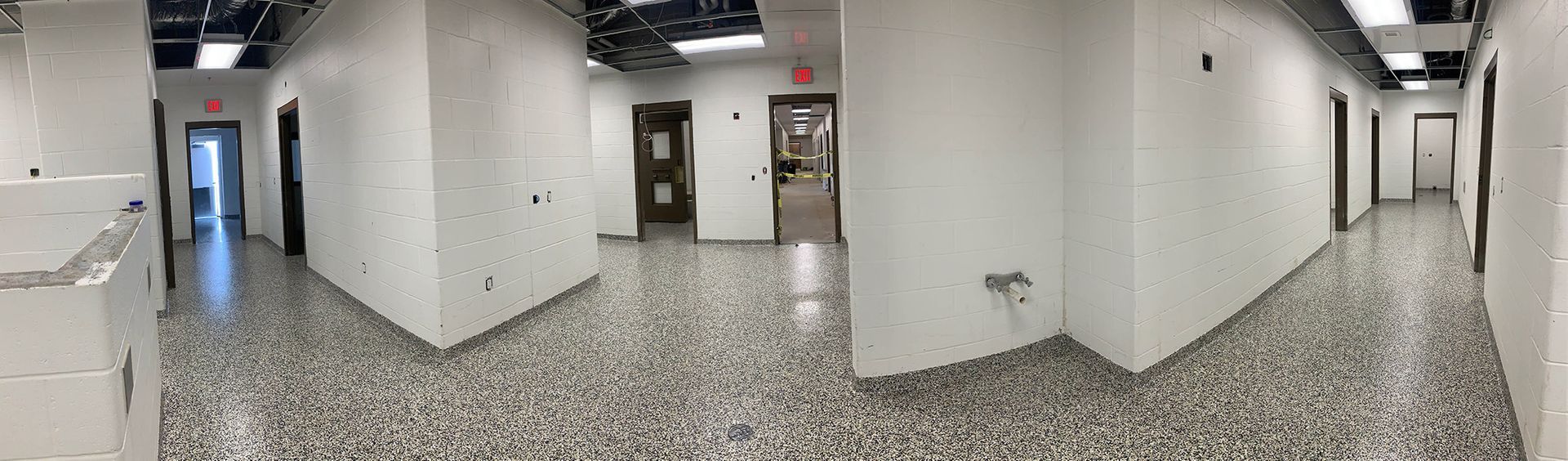 Empty hallway with white walls, terrazzo floor, and elevator doors at the end of the corridor