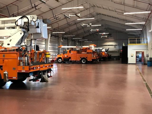 Orange utility trucks parked inside a large maintenance garage with a high arched ceiling