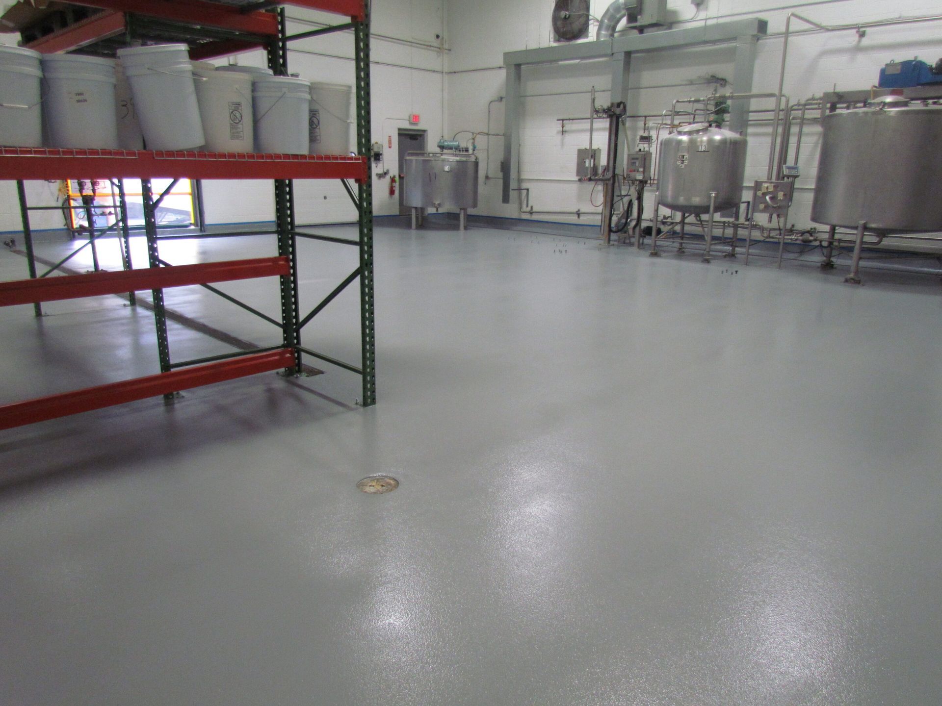 Empty industrial room with metal shelving, tanks, and a gray concrete floor