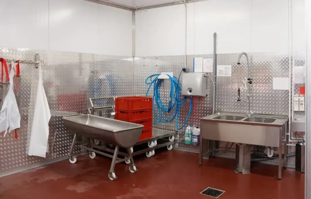 Stainless steel industrial wash station with sinks, hoses, towels, and a wheeled table in a tiled room