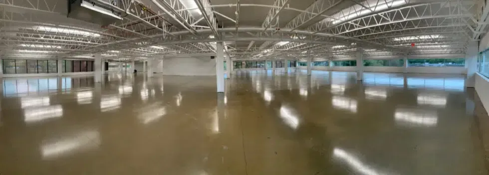 Empty indoor sports hall with glossy floor, exposed ceiling trusses, and windows along the walls