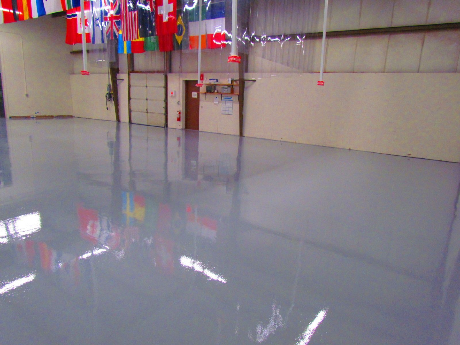 Empty indoor hall with a glossy gray floor, beige walls, and colorful flags hanging from the ceiling.
