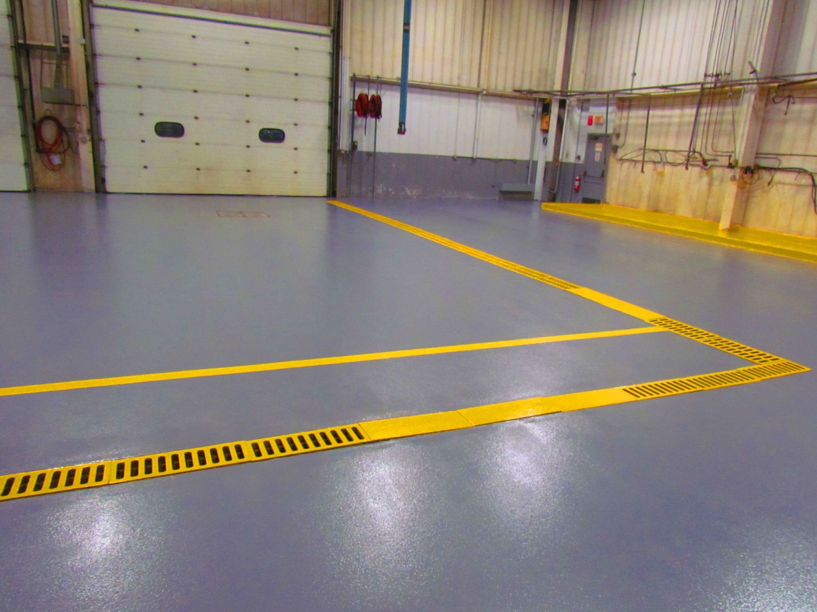 Empty industrial garage with gray floor, yellow safety lines, and a large closed overhead door.